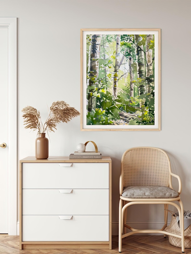 May include: A framed watercolor painting of a forest scene with tall trees and green foliage. The painting is in a light wood frame and is hanging on a white wall.