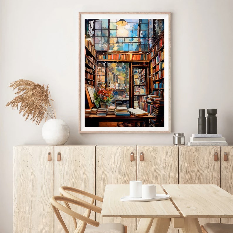 May include: A watercolour painting of a bookstore interior with a large window, wooden shelves filled with books, and a table with books on it. The painting is framed in a light wood frame.