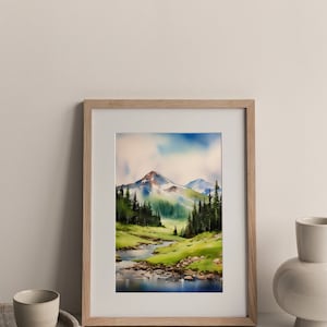 May include: A framed watercolour painting of a mountain landscape with a river flowing through a valley. The mountains are green and brown with snow-capped peaks. The river is blue and reflects the sky. The painting is set against a white background.