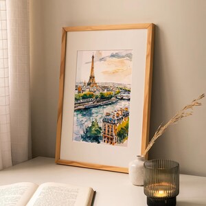 Puede incluir: Una pintura de acuarela enmarcada de la Torre Eiffel en Par&iacute;s, Francia. La pintura muestra la torre desde la distancia, con el r&iacute;o Sena y otros edificios en primer plano. La pintura est&aacute; en un marco de madera y est&aacute; colgada en una pared blanca.