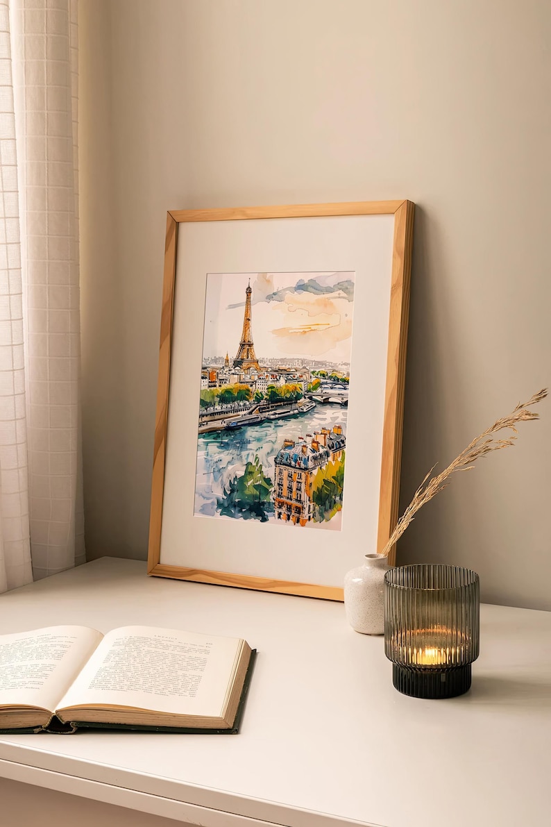Puede incluir: Una pintura de acuarela enmarcada de la Torre Eiffel en Par&iacute;s, Francia. La pintura muestra la torre desde la distancia, con el r&iacute;o Sena y otros edificios en primer plano. La pintura est&aacute; en un marco de madera y est&aacute; colgada en una pared blanca.
