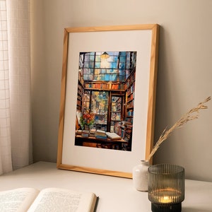 May include: A framed watercolour painting of a bookstore interior with bookshelves filled with books, a wooden desk with books and a vase of flowers, and a window with a view of a street. The painting is in a light wood frame and is hanging on a white wall.