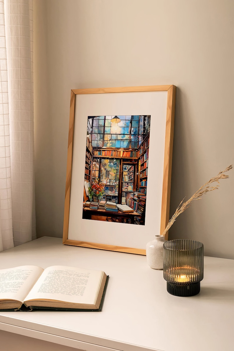 May include: A framed watercolour painting of a bookstore interior with bookshelves filled with books, a wooden desk with books and a vase of flowers, and a window with a view of a street. The painting is in a light wood frame and is hanging on a white wall.