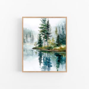 May include: A watercolour painting depicting a tranquil lake scene with evergreen trees and their reflections in the water. The artwork is framed in a light wood frame, creating a calming and natural aesthetic. The colour palette includes shades of green, blue, and brown.