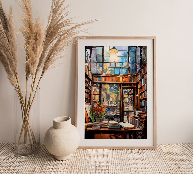 May include: A framed watercolour painting of a bookstore interior. The bookstore is filled with bookshelves and stacks of books. A large window in the back of the store shows a view of a street outside. The painting is in a light wood frame.