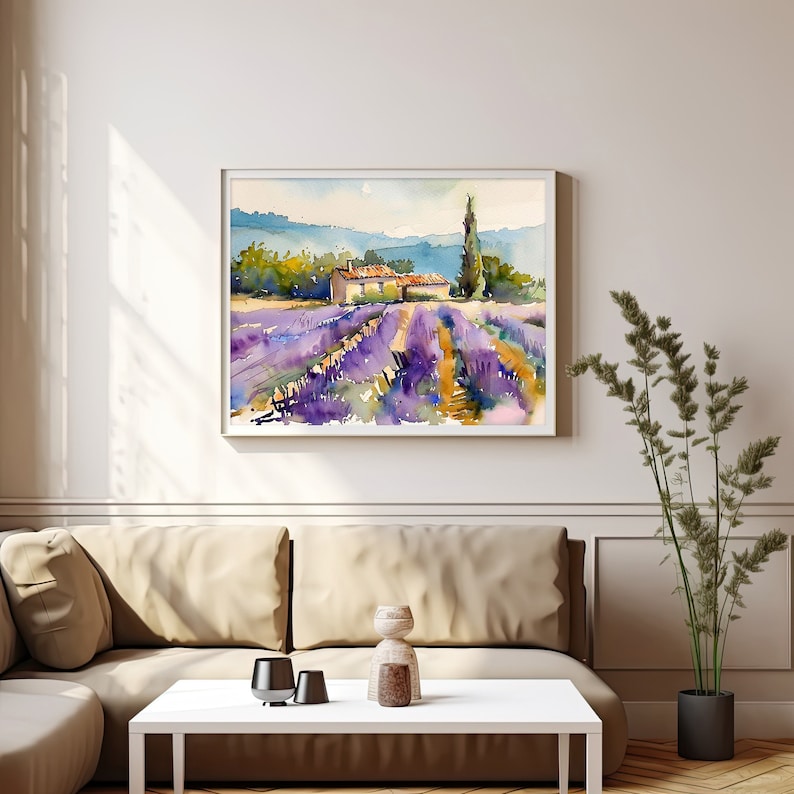 K&ouml;nnte beinhalten: Ein Aquarellbild eines Lavendelfeldes mit einem kleinen Haus und einem hohen Baum im Hintergrund. Das Bild ist in einem wei&szlig;en Rahmen gerahmt und h&auml;ngt an einer wei&szlig;en Wand.