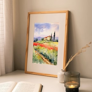 May include: A framed watercolor painting of a house in a field of red flowers with a path leading to it. The house is yellow with a red roof and there are two green trees in the background. The painting is in a wooden frame.