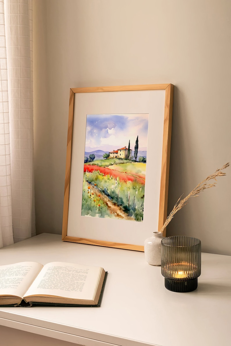 May include: A framed watercolor painting of a house in a field of red flowers with a path leading to it. The house is yellow with a red roof and there are two green trees in the background. The painting is in a wooden frame.
