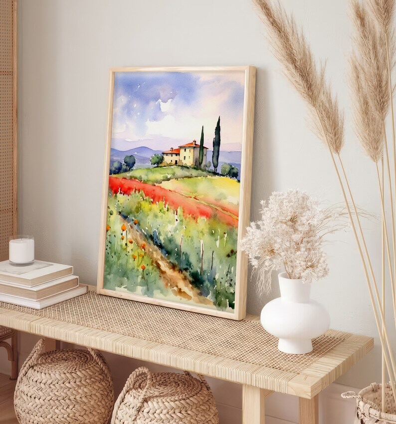 May include: A watercolor painting of a yellow house with a red roof in a field of red and yellow flowers. The house is surrounded by green trees and a blue sky with white clouds. The painting is framed in a light wood frame.