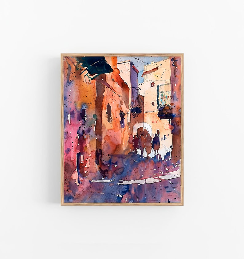 May include: Watercolor painting of a sunlit street scene with buildings in shades of orange, pink, and blue. The artwork is framed in a light wood frame. Figures are silhouetted in the archway.