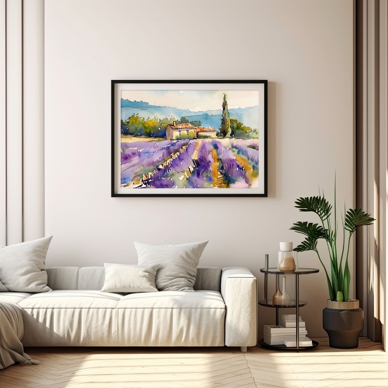 K&ouml;nnte beinhalten: Ein Aquarellbild eines Lavendelfeldes mit einem kleinen Haus und einem hohen Baum im Hintergrund. Das Bild ist in Schwarz gerahmt und h&auml;ngt an einer wei&szlig;en Wand.