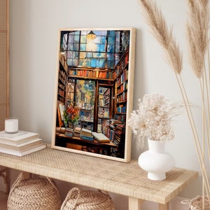 May include: A painting depicting the interior of a bookshop, featuring a large window, shelves overflowing with books, and a wooden table piled high with books. The painting is framed in a light wood frame and hangs on a white wall.