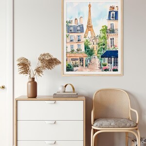 May include: A watercolour painting depicting a Parisian street scene with the Eiffel Tower in the background. The painting features buildings with balconies, trees, and a cafe with a blue awning.