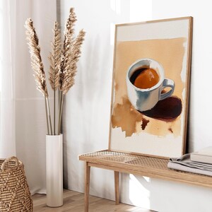 Puede incluir: Una pintura de acuarela enmarcada de una taza de caf&eacute; blanca con caf&eacute; marr&oacute;n sobre un fondo beige.
