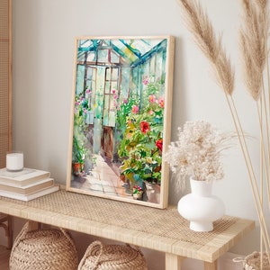 Puede incluir: Una pintura de acuarela de un invernadero lleno de vegetaci&oacute;n exuberante y flores rosas vibrantes. La pintura est&aacute; enmarcada en un marco de madera clara y cuelga de una pared blanca sobre un banco de madera.