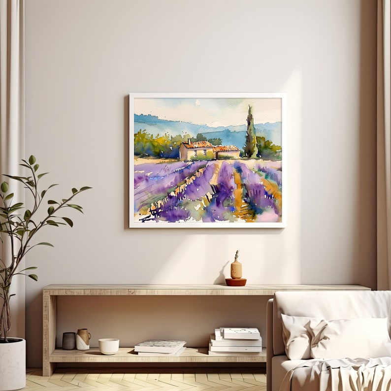K&ouml;nnte beinhalten: Ein Aquarellbild eines Lavendelfeldes mit einem kleinen Haus und einem hohen Baum im Hintergrund. Das Bild ist in einem wei&szlig;en Rahmen gerahmt.