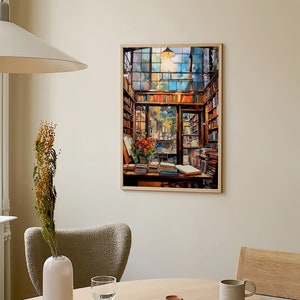 May include: A framed painting depicting the interior of a bookshop, featuring a large window, wooden shelves stacked with books, and a table with books and a vase of flowers. The painting is in a light wood frame and is hanging on a beige wall.
