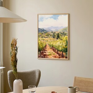 May include: A framed watercolor painting of a vineyard landscape with rolling hills, green vines, and a dirt path leading through the center. The painting is in a light wood frame and hangs on a beige wall.
