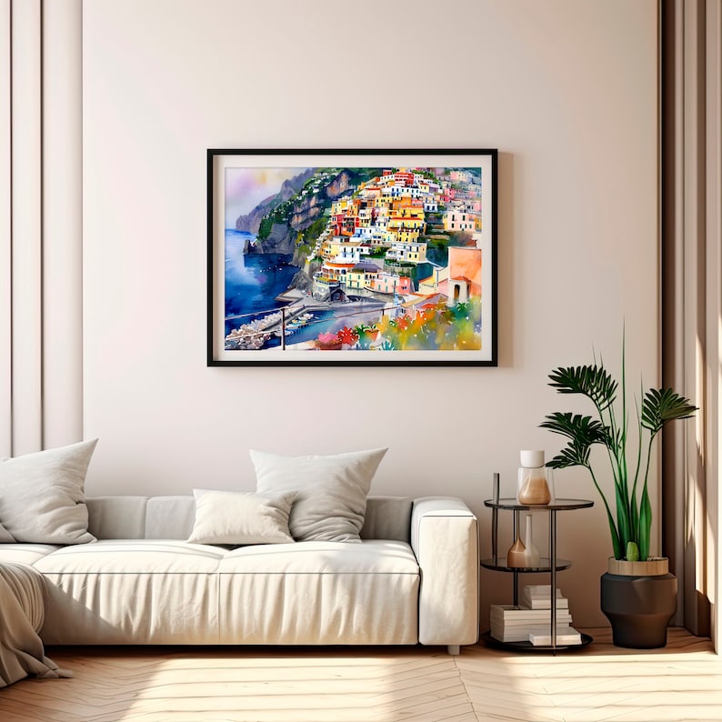 May include: Watercolour painting of a colourful Italian village on a cliffside overlooking the sea. The painting features a variety of buildings, including houses, shops, and a church. The sea is a deep blue, and the sky is a light blue. The painting is framed in black.