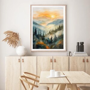 May include: Watercolor painting of a mountain landscape with a sunset. The artwork features layers of blue and green mountains, with a bright orange and yellow sky. The painting is framed in a light wood frame.