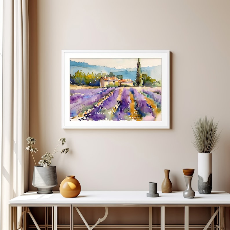 K&ouml;nnte beinhalten: Ein Aquarellbild eines Lavendelfeldes mit einem kleinen Haus und einem hohen Baum im Hintergrund. Das Bild ist in einem wei&szlig;en Rahmen gerahmt und h&auml;ngt an einer Wand.