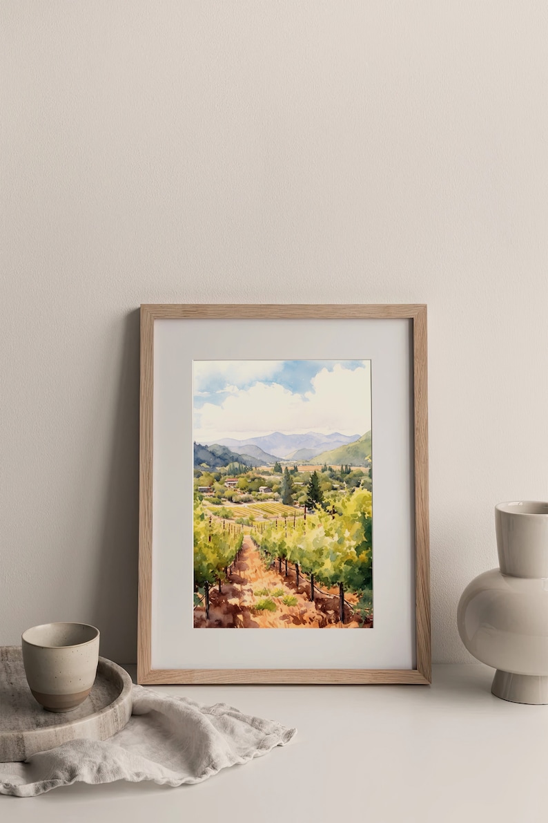 May include: A framed watercolor painting of a vineyard landscape. The painting depicts a winding path through rows of grapevines, with a small village in the distance. The sky is a light blue with fluffy white clouds.