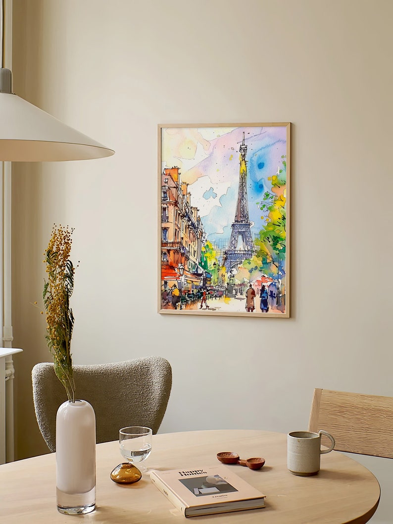 Puede incluir: Una pintura de acuarela enmarcada de la Torre Eiffel en Par&iacute;s, Francia. La pintura representa una escena de calle con edificios, &aacute;rboles y personas caminando. El cielo es azul claro con nubes rosadas y amarillas.