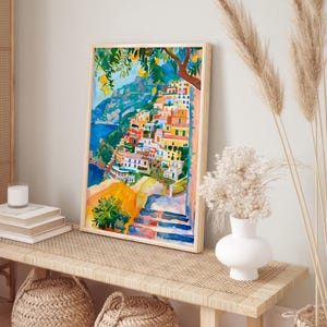 May include: Watercolour painting depicting a coastal Italian village with vibrant buildings, a blue sea, and a lemon tree. The artwork is framed in a light wood frame and displayed on a woven bench with decorative baskets.