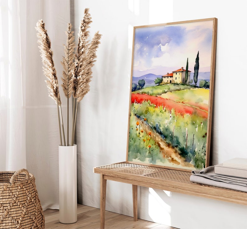May include: A watercolor painting of a yellow house with a red tiled roof in a field of red flowers. The house is surrounded by green trees and a blue sky with white clouds. The painting is framed in a light wood frame.