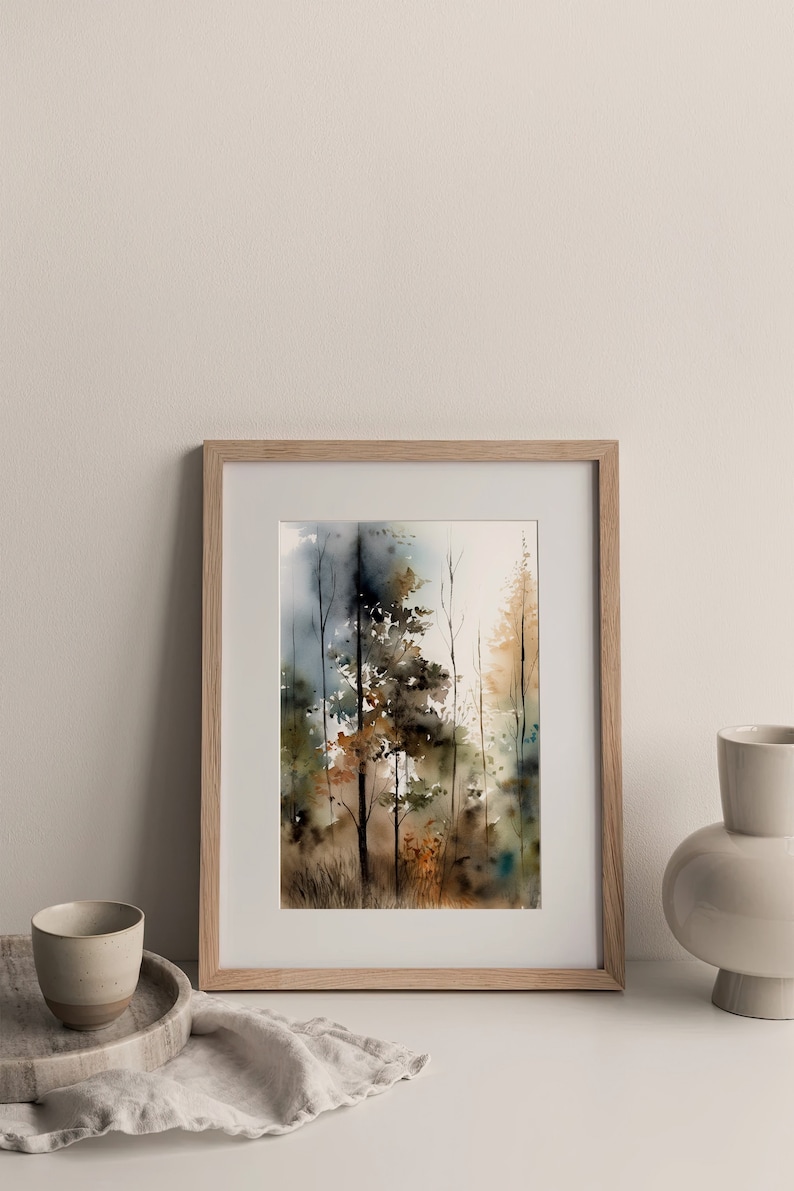May include: A framed watercolor painting of a forest scene with trees in shades of brown, green, and blue. The painting is in a light wood frame and is sitting on a white surface.