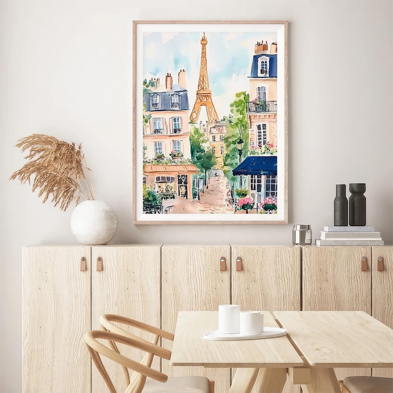 May include: A watercolour painting of a Parisian street scene with the Eiffel Tower in the background. The painting features buildings with blue and white accents, a cafe with a blue awning, and trees.