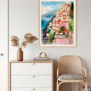 May include: A watercolour painting depicting colourful buildings perched on a cliff overlooking the sea. The buildings are painted in shades of pink, yellow, orange, and red. The sea is a deep blue, and the sky is a light blue with white clouds.