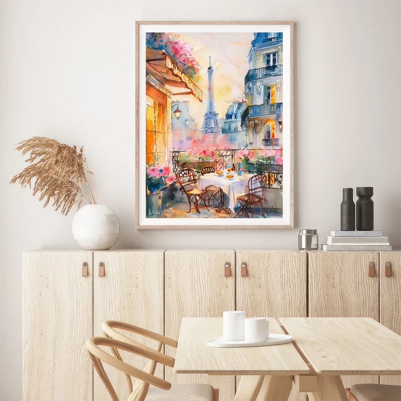 May include: A watercolor painting of a Parisian balcony scene with a view of the Eiffel Tower. The balcony has a table set for two with white chairs and a white tablecloth. There are flowers and greenery in pots on the balcony.