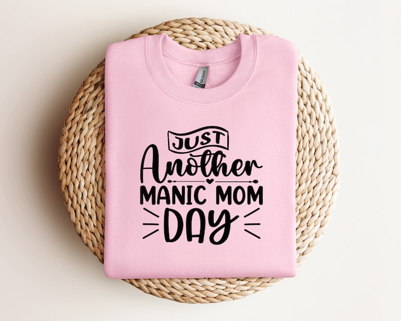 May include: Pink sweatshirt with black text that reads "Just Another Manic Mom Day" with a heart symbol.