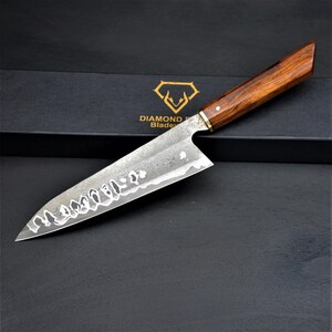 May include: A chef's knife with a wooden handle and a textured blade. The knife has a dark brown handle and a silver blade with a decorative pattern. The knife is set against a black background with the words "DIAMOND Blade" and a diamond logo.