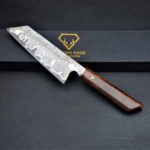 May include: A Damascus steel chef's knife with a dark wood handle. The blade has a unique pattern, and the handle is a rich brown color. The knife is displayed on a black surface, with the words "DIAMOND EDGE WORKS" visible.