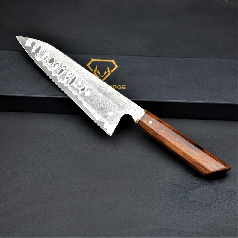 May include: A stainless steel chef's knife with a dark wood handle. The blade has a unique pattern and a sharp edge. The handle is a rich brown color with a brass bolster. The knife is designed for professional or home use.