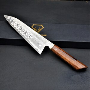 May include: A stainless steel chef's knife with a patterned blade and a dark wood handle. The knife is angled, showcasing the blade's design and the handle's rich color. The knife is set against a black background.