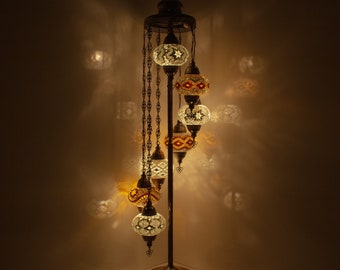 Może przedstawiać: Lampa stojąca o spiralnym wzorze z sześcioma kolorowymi kulami z mozaikowego szkła. Lampa wykonana jest z metalu i ma złote wykończenie.