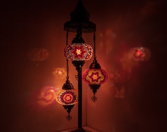 May include: A three-light floor lamp with a traditional design. The lamp has a black metal base and three round, colorful mosaic glass shades. The shades are lit and cast a warm glow.