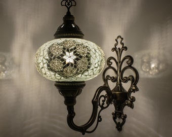 May include: A white mosaic glass globe wall sconce with a decorative metal scrollwork bracket. The sconce is lit and casting a warm glow.