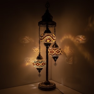 May include: A three-light floor lamp with a dark bronze finish and three round mosaic glass shades. The shades are decorated with geometric patterns in shades of red, yellow, blue, and green.