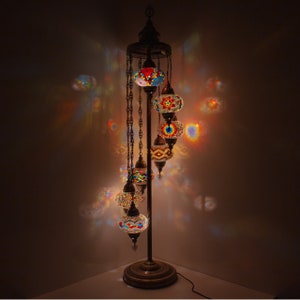 May include: A tall, ornate floor lamp with a chain-link design and six colorful mosaic glass globes. The globes are lit from within, casting a warm glow.