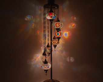 May include: A tall, ornate floor lamp with a chain-link design and six colorful mosaic glass globes. The globes are lit from within, casting a warm glow.