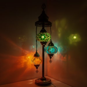 May include: A three-light floor lamp with a traditional design. The lamp has a metal base and three hanging globes with intricate mosaic patterns in shades of green, blue, and orange.