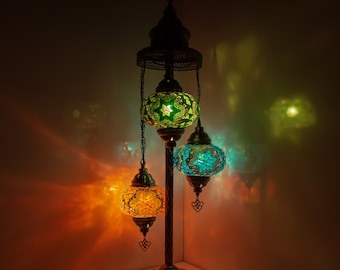 Puede incluir: Una lámpara de pie de tres luces con un diseño tradicional. La lámpara tiene una base de metal y tres globos colgantes con intrincados patrones de mosaico en tonos de verde, azul y naranja.