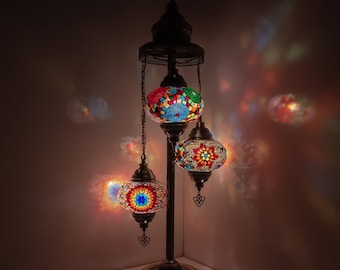 May include: A three-light floor lamp with a dark metal base and three colorful mosaic glass globes. The globes are lit and cast a warm glow.