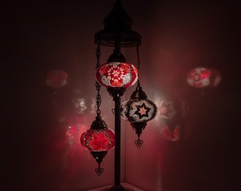 May include: A three-light floor lamp with a black metal base and three colorful mosaic glass globes. The globes are red, white, and black with geometric patterns. The lamp is lit and casting a warm glow.