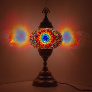 May include: A colourful mosaic table lamp with a star-shaped design. The lamp is made of glass and metal and has a warm, inviting glow.