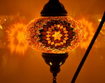 May include: A mosaic glass lamp with a star-shaped design in shades of orange, red, and yellow. The lamp is hanging from a black metal stand.